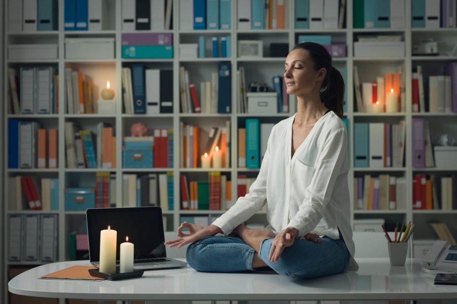 Relaxed woman practicing meditation at home at night, she is sitting in the lotus position on the office desk